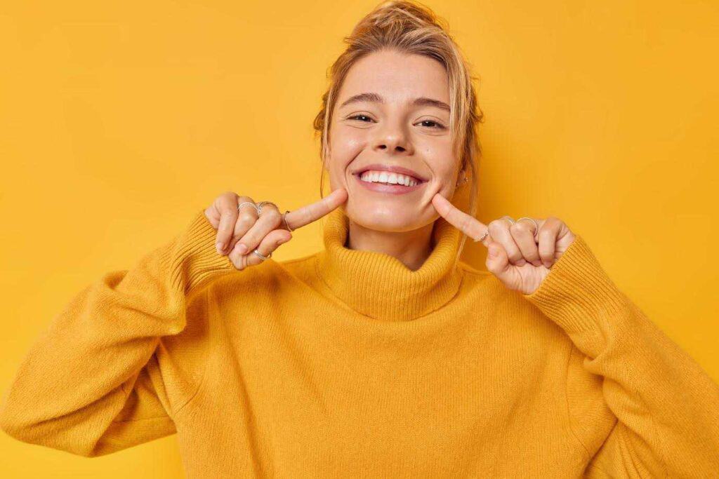 Young Girl Showing her Teeth with Pointing Finger in Yellow Background | Smile Virtual