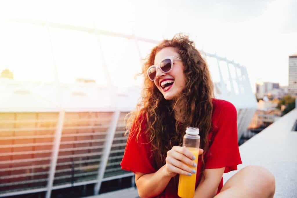 Happy Young Female Holding Juice Bottle and Sitting on Terrace | Smile Virtual